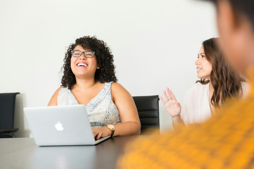 Woman smiling while working at a laptop in a bright home office, suggesting focused, positive work and well-being.